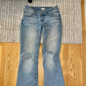 Nelly Bootcut jeans med slitna knän - Ljusblå bootcut jeans från Nelly med slitningar och hål på båda knäna. Klassisk femficksmodell med låg midja och snygga detaljer på bakfickorna. Jeansen är i storlek 36 och är tillverkade i mjukt denimtyg. Priset går att diskutera😍