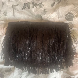 Svart fransig paljett tubtopp S - Supersnygg svart tubtopp med massor av paljettfransar som ger en riktigt cool och glittrig look. Perfekt för dig som vill sticka ut och fånga allas blickar. Toppens material är syntet och den är axelbandslös. En typ av korsettop med dragkedja.