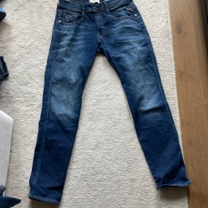 Blå Replay jeans, midwaist, straight fit - Snygga blå jeans från Replay med klassisk femficksdesign och coola slitningar. Modellen är anbass. Jeansen är tillverkade i denim och har detaljerade bakfickor med kontrastsömmar. Perfekta för en avslappnad och trendig look.