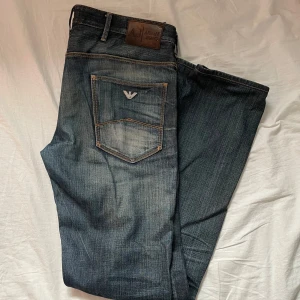 Armani Jeans blå denimjeans - Säljer ett par snygga mörka jeans från Armani Jeans . Jeansen har läderpatch med logga bak och silverfärgad Armani-detalj på fickan. De är raka/slim fit i modellen och har kontrastsömmar för en cool look. Storlek 31/34 men är lite korta för mig som är 193cm 77kg, skulle säga att de passar någon som är 185-190 som bäst. 