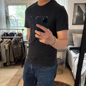 Svart t-shirt från Tommy Jeans - Svart t-shirt från Tommy Jeans med klassisk passform och liten broderad logga på bröstet. Tillverkad i mjuk bomull och har rund halsringning samt korta ärmar. Perfekt basic-plagg med stilren vibe.