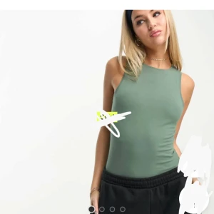 Grön ärmlös bodysuit från New Look - Säljer en stilren grön bodysuit från New Look. Modellen är ärmlös med hög halsringning och tight passform, perfekt att styla med jeans eller kjol. Gjord i mjuk bomull som känns skön mot huden. Enkel och clean look som funkar till många outfits.