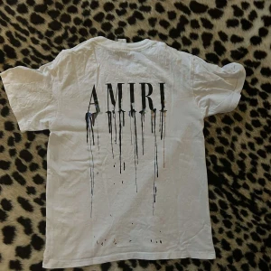 Amiri - T-Shirt - Vit t-shirt från Amiri med svart logotyp och coolt drip-tryck både fram och bak. Klassisk rund hals och korta ärmar. Skön passform och stilren design som sticker ut med den unika grafiska detaljen. Perfekt tröja nu inför sommaren. Tröjan är nästan i nyskick, pris går att diskutera vid snabb affär💧