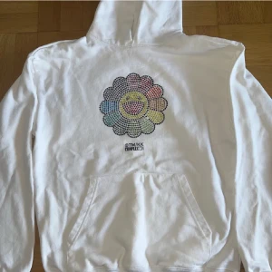 Vit Rhinestone hoodie  - Vit hoodie med stor färgglad blomma i strass på bröstet. Klassisk känguruficka och huva. Perfekt statement-plagg för dig som gillar streetwear och unika samarbeten.