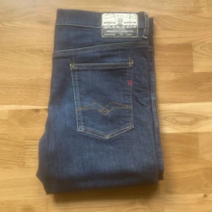 Replay jeans  - Säljer ett par Replay jeans i mörkblå tvätt med klassiska kontrastsömmar och femficksdesign. Jeansen har slim passform och raka ben, tillverkade i stretchig bomullsdenim för skön känsla. Snygg Replay-patch bak i midjan.