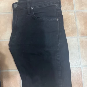 Svarta Lee  jeansbyxor  W31 L30  Slim - Svarta jeansbyxor från Lee i klassisk femficksmodell. Byxorna har normal passform och är tillverkade i ett mjukt denimtyg. Perfekta för dig som gillar stilrena och enkla jeans.