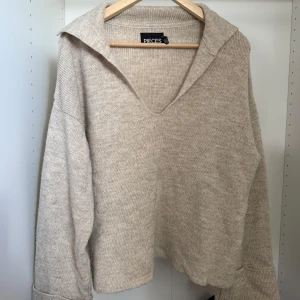 Beige stickad tröja med krage från Pieces - Mysig beige stickad tröja från Pieces med v-ringning och bred krage. Tröjan har lång ärm och en avslappnad passform. Fint skick!💕