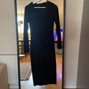 Svart långklänning med twistdetalj från Gina Tricot - Säljer en svart långklänning från Gina Tricot med lång ärm och snygg twistdetalj framtill. Klänningen har en figurnära passform och är perfekt för dig som gillar stilrena plagg med en twist.