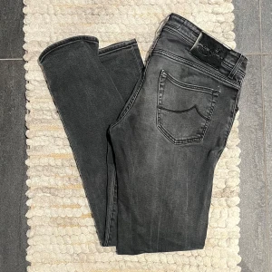 Jacob Cohën Jeans Mörkgråa - Exklusiva mörkgrå jeans från Jacob Cohën, storlek 35 men passar mer som en 33 i midjan. Lite slitna vid skrevet, men i övrigt väldigt fint skick. Diskreta, designade slitningar vid låren ger en lyxig och avslappnad look.