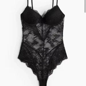 Svart spetsig bodysuit med bygel - Säljer en svart bodysuit i spets med bygel och justerbara axelband. Bodyn har knäppning i grenen och vackra spetsdetaljer över hela plagget. Perfekt för att känna sig extra snygg och självsäker. Storlek 80 C, skulle säga att den sitter bra på 75 B då den är liten i storleken 