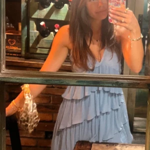 Ljusblå volangklänning med omlott - Säljer en söt ljusblå klänning med flera volanglager och omlottkänsla. Klänningen är ärmlös och har en luftig, flowy passform som passar perfekt till sommaren. Perfekt för dig som gillar romantisk och feminin stil.