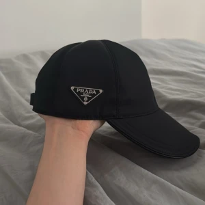 Svart keps från Prada - Säljer en stilren svart keps från Prada med klassisk böjd skärm och justerbart spänne bak. Kepsen har diskret Prada-logga på sidan och är tillverkad i ett slätt, syntetiskt material. Perfekt accessoar för en clean och modern look.  Pris kan diskuteras vid snabb affäer 📬🚚🚛 hör av er i dm för mer info, äkta men ingen box elle nåt