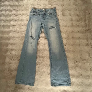 Ljusblå slitna jeans med raka ben - Säljer ett par ljusblå jeans som är bootcut och low waist. Dom är lite för stora på mig som är 166 men också storlek 164. 2 hål där fram. Bra skick men använder inte! 
