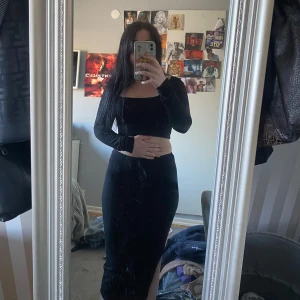 Svart ribbad tvådelad klänning - Säljer en svart tvådelad klänning med långärmad croppad topp och hög midjad kjol med slits. Setet är ribbat och har en tight passform, perfekt för dig som gillar stilrena och trendiga plagg.