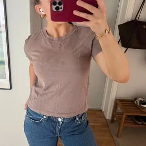 Mauve t-shirt från Zara - En basic mauve-färgad t-shirt från Zara med rund halsringning och korta ärmar. Perfekt till jeans eller kjol för en enkel och stilren look. Tillverkad i mjuk bomull som känns skön mot huden.