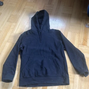 Svart hoodie från Jack & Jones - Säljer en svart hoodie från Jack & Jones med klassisk huva och magficka. Tröjan har långa ärmar och en enkel, stilren design utan tryck eller mönster. Perfekt för en avslappnad stil.