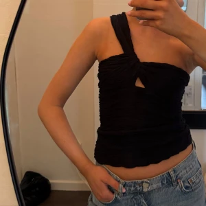 Svart oneshoulder topp med twistad detalj - Svart oneshoulder topp i rynkat material med twistad detalj framtill. 
