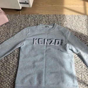Ljusblå/grå sweatshirt från Kenzo - Säljer en ljusblå/grå sweatshirt från Kenzo med stor logotyp i svart och vitt på bröstet. Tröjan har rund halsringning och långa ärmar. 