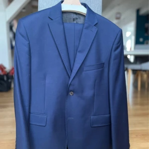 Vistula kostym - En klassisk elegant kostym från Vistula i mörkblå. Smal modell, perfekt för formell styling - bröllop, jobbintervju, fest eller arbete.   Skick: mycket bra, använd ett fåtal gånger och inga fläckar eller skador.   Storlek: 52 S (höjd 170cm, bröstvidd 104cm, midja 90cm) Stil: Smal Material:    - Tyg: 100% ull    - Foder: 100%viskos  Egenskaper:   - Kavajen knäpps med två knappar  - Två fickor med flikar (fortfarande fastsydda som i en ny produkt) + en bröstficka.  - Byxor med sido- och bakfickor