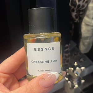 ESSNCE Carashmellow Eau de Parfum - Parfymflaska med transparent glas och svart cylinderformad kork. Innehållet är ljusgult och etiketten är vit med svart text. Doften heter Carashmellow och är en Eau de Parfum.