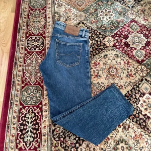 Jacob Cohën jeans Nick - Säljer ett par klassiska blå jeans från Jacob Cohën med raka ben och  slim passform. Storlek 34/30. Jeansen har fem fickor, läderpatch med logga bak och är tillverkade i ett robust denimtyg. Jeansen är uppsydda