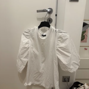 Vit topp med puffärmar från H&M - Säljer en vit topp från zara med trendiga puffärmar och rund halsringning. Toppens material känns mjukt och lätt, perfekt för att lyfta en enkel outfit. Passformen är normal och ärmarna är långa med extra volym vid axlarna.