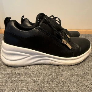 Svarta sneakers med vit sula och dragkedja - Snygga svarta sneakers med tjock vit platt sula och svarta snören. Skorna har dragkedja i sidan med gulddetalj för extra stil. Perfekta för en sportig och trendig look. 1 gång använda helt nya!!!