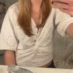Vit broderad omlottblus - Superfin vit omlottblus med broderade hålmönster och puffärmar. Blusen har knyt framtill och är croppad, perfekt till både jeans och kjol. Ger en fräsch och somrig look!