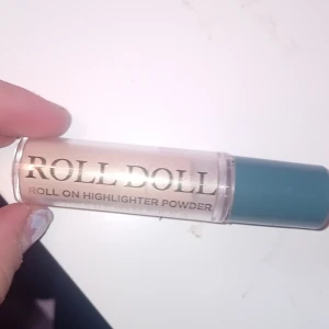 Roll Doll Roll On Highlighter Powder - Roll-on highlighter i puderform från Makeup Mekka. Ger en skimrande, ljus champagnefärgad glow. Smidig applikator med blått lock, perfekt för att highlighta kindben, näsrygg och amorbåge.