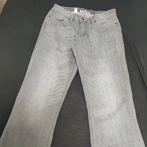 Ljusgrå jeansbyxor - Säljer ett par ljusgrå jeansbyxor med klassisk femficksdesign och raka ben. Byxorna har normal passform och stängs med dragkedja och knapp. Perfekta för en avslappnad och stilren look.