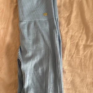 Ljusblå ribbade tights från Drop of Mindfulness -  ljusblå ribbade tights från Drop of Mindfulness. Hög midja och stretchigt material som sitter skönt på kroppen. Perfekta för träning. Diskret logga i metall framtill.