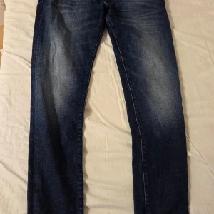 Mörkblå jeans från Diesel D-Strukt - Säljer ett par mörkblå Diesel D-Strukt jeans i slim fit. Jeansen har klassisk femficksdesign och snygga slitningar framtill. Perfekta för dig som gillar en smalare passform och stilren look.