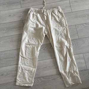 Beiga linnebyxor från H&M - Säljer ett par beiga linnebyxor från H&M med regular fit. Byxorna har resår i midjan och sidofickor, perfekta för varma dagar. Lätta och luftiga med avslappnad passform.
