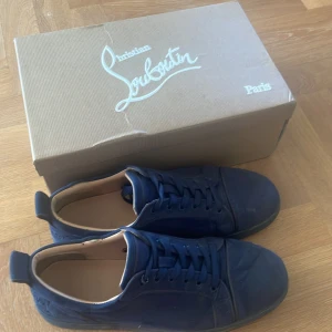 Mörkblå sneakers från Christian Louboutin - Säljer ett par mörkblå sneakers från Christian Louboutin med klassisk röd sula och diskret logga på sidan. Skorna har snörning och är tillverkade i mocka. Kommer med originalkartong, dustbags och äkthetskort. Priset går att diskutera, byten går bra med