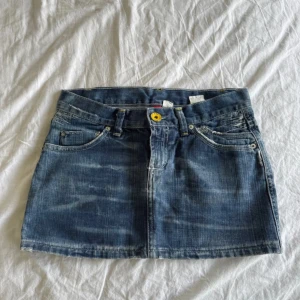Jeanskjol med slitna detaljer - Säljer en klassisk blå jeanskjol med slitna bakfickor och gul knapp framtill. Kjolen är lågmidjad och inga defekter❤️‍🔥