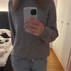 Grå stickad tröja - Mysig grå stickad tröja med rund halsringning och långa ärmar. Perfekt för kyligare dagar och enkel att matcha med olika outfits. Klassisk och stilren design.