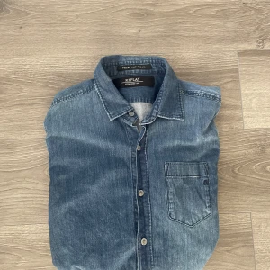Jeansskjorta från Replay - Säljer en klassisk blå jeansskjorta från Replay med bröstficka och knappar framtill. Skjortan har en normal passform och är långärmad, perfekt för en avslappnad stil. Tidlös design med diskret logga på fickan. Storlek S med skön passform. Hör av dig vid minsta fundering🙌😊