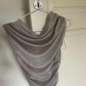Silverfärgad glittrig topp från Zara - Säljer en snygg silverfärgad topp från Zara i storlek S. Toppen har glittrigt material och en draperad, omlottliknande urringning. 