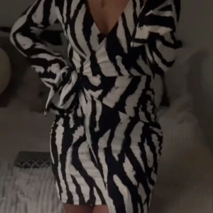 Zebramönstrad omlottklänning med knytband - Säljer en snygg kort omlottklänning med zebramönster i svart och vitt. Klänningen har långa ärmar och ett knytband i midjan som framhäver figuren. Endast använd 1 gång. Från Gina tricot. 