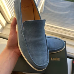 Blå loafers från Loake - Snygga blå loafers från Loake i mocka med en stilren design. Skorna har en rund tå och en ljus sula som ger en fräsch look. Perfekta för en avslappnad men ändå elegant stil. Helt nya endast testade, köpta för 2499 men säljer för 1599