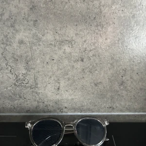 Transparenta solglasögon med runda linser - Snygga solglasögon med transparent båge och runda, mörka linser. Perfekta för en stilren look. Passar både till stranden och stadspromenaden.