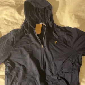 Mörkblå jacka med huva från Next - Jag säljer en super snygg oanvänd hoodie ifrån märket Next. Den är i storlek M och har även en liten brodering på framsidan. Skriv om du vill ha fler bilder!