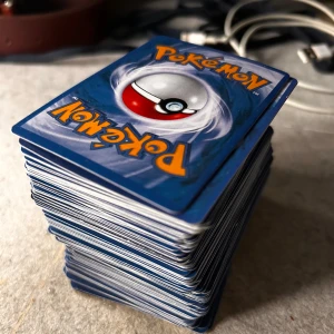 Samling Pokémonkort - Stor samling Pokémonkort med olika motiv och färger. Perfekt för samlare eller spelentusiaster. Kortens baksida har den klassiska blå designen med en Pokéball i mitten.