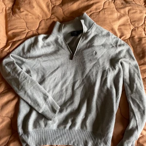 Grå tröja från Polo Ralph Lauren - Säljer en stilren grå tröja från Polo Ralph Lauren i mjuk pima bomull. Tröjan har en dragkedja vid halsen och långa ärmar. Perfekt för en avslappnad och snygg look. Bakåtlutande tröja. Står för frakt. Ny ca 2000+