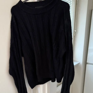 Svart stickad tröja från Monki - Säljer en svart stickad tröja från Monki. Tröjan har en ribbad design och långa ärmar, perfekt för kyligare dagar. Enkel och stilren, passar till det mesta. Hör av dig vid intresse!