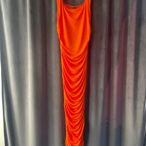 Orange ärmlös klänning - Snygg orange ärmlös klänning med draperad design. Perfekt för en färgstark look. Klänningen har en lång och elegant siluett.