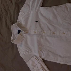 Vit skjorta från Ralph Lauren - Säljer en klassisk vit skjorta från Ralph Lauren med broderad logga på bröstet. Skjortan har långa ärmar och knappar framtill. 