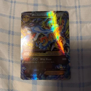 M Charizard EX Pokémonkort - Säljer ett M Charizard EX Pokémonkort med holografisk yta. Kortet har en kraftfull design med Charizard i fokus och texten 'Wild Blaze' som attack. Perfekt för samlare eller spelare som vill förstärka sin kortlek.