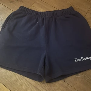 Mörkblå shorts med tryck - Säljer ett par mörkblå mjukisshorts med elastisk midja och trycket 'The Hamptons' på ena benet. Perfekta för en avslappnad dag.