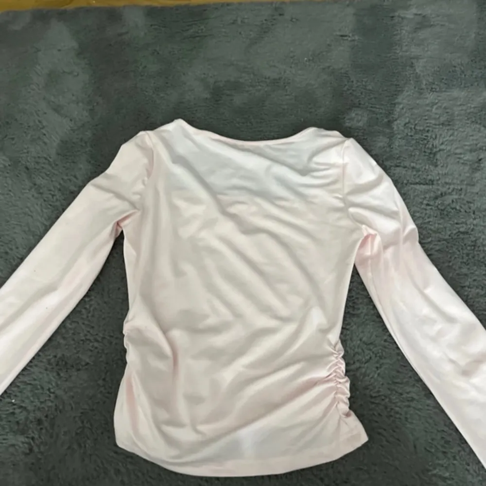 Säljer en söt ljusrosa långärmad topp med rynkade detaljer på sidorna. Toppen har en fyrkantig halsringning och är gjord i ett mjukt material. Perfekt för en stilren look! I storlek XS/S, aldrig använd är i ny skick.. Neuletakit & Villapaidat.